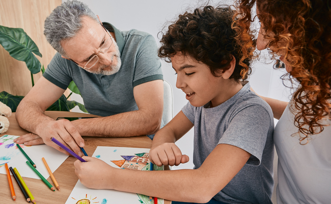 child smiling and drawing with parent and therapist