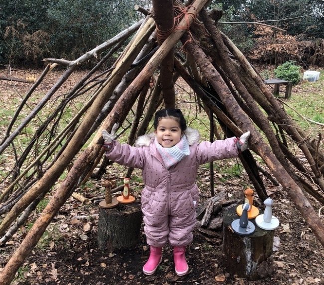 A young child standing in a den made of sticks