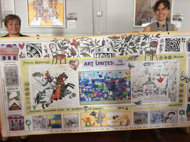Two women holding up the combined art work in a school hall.