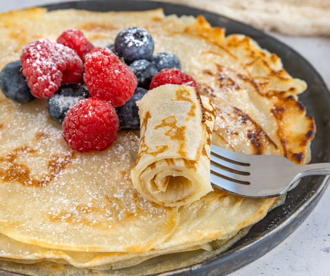 Pancakes on a black plate with powdered sugar, raspberries, and blueberries