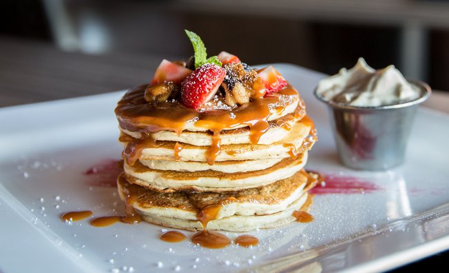 A stack of pancakes with fruit on top and a small bowl of cream