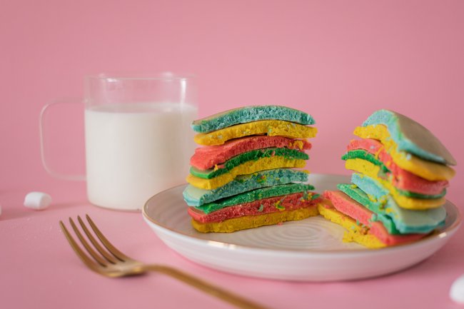 Glass of milk with rainbow stack of pancakes on a plate cut in half